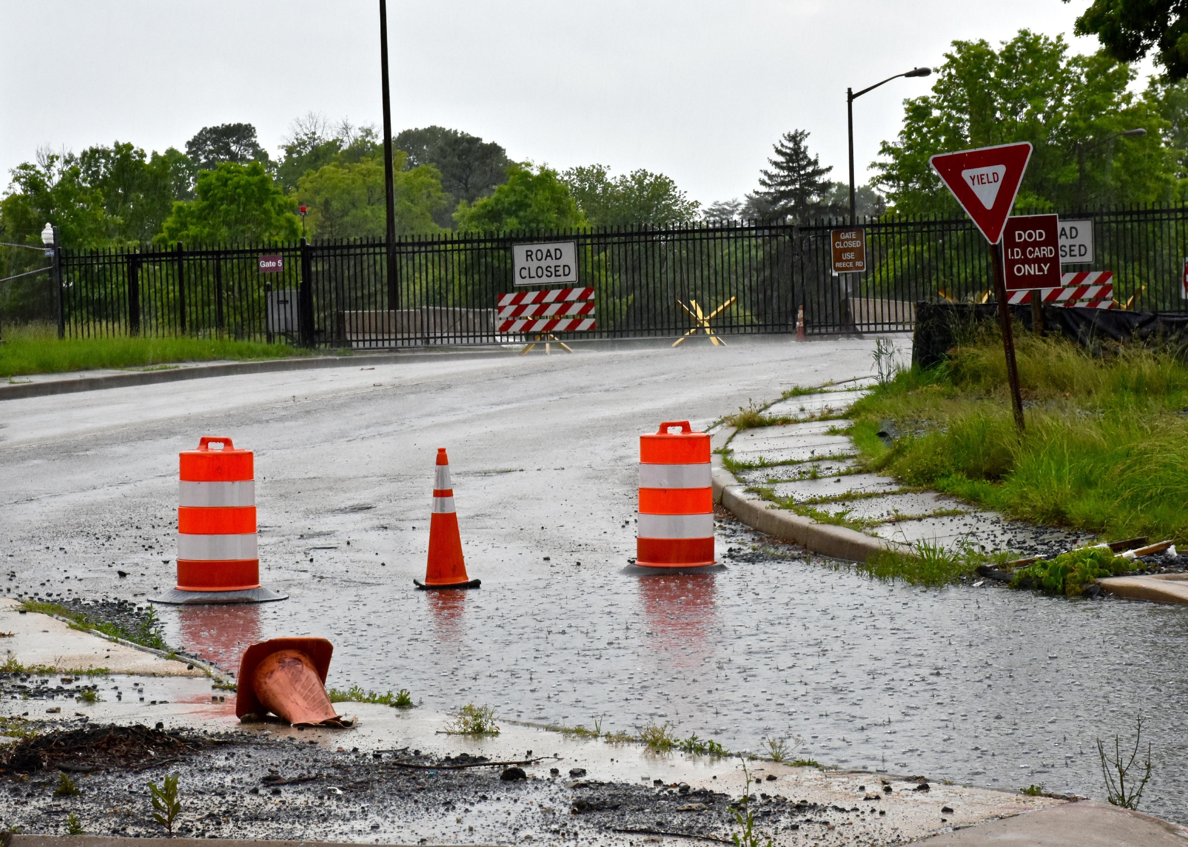 A flooded road with traffic cones and a closed gate on a private installation.