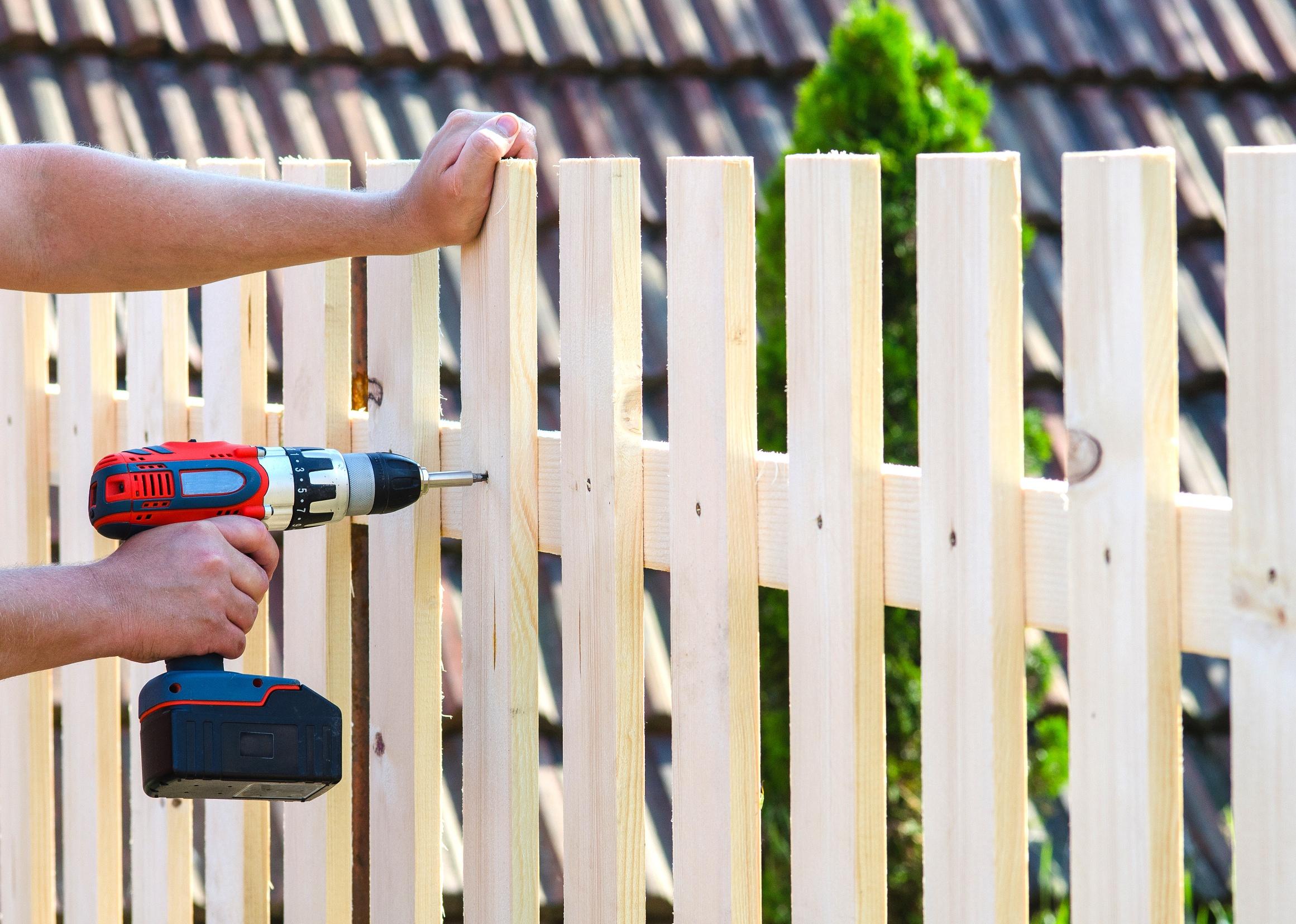 Person building a wooden fence with a drill and screw.