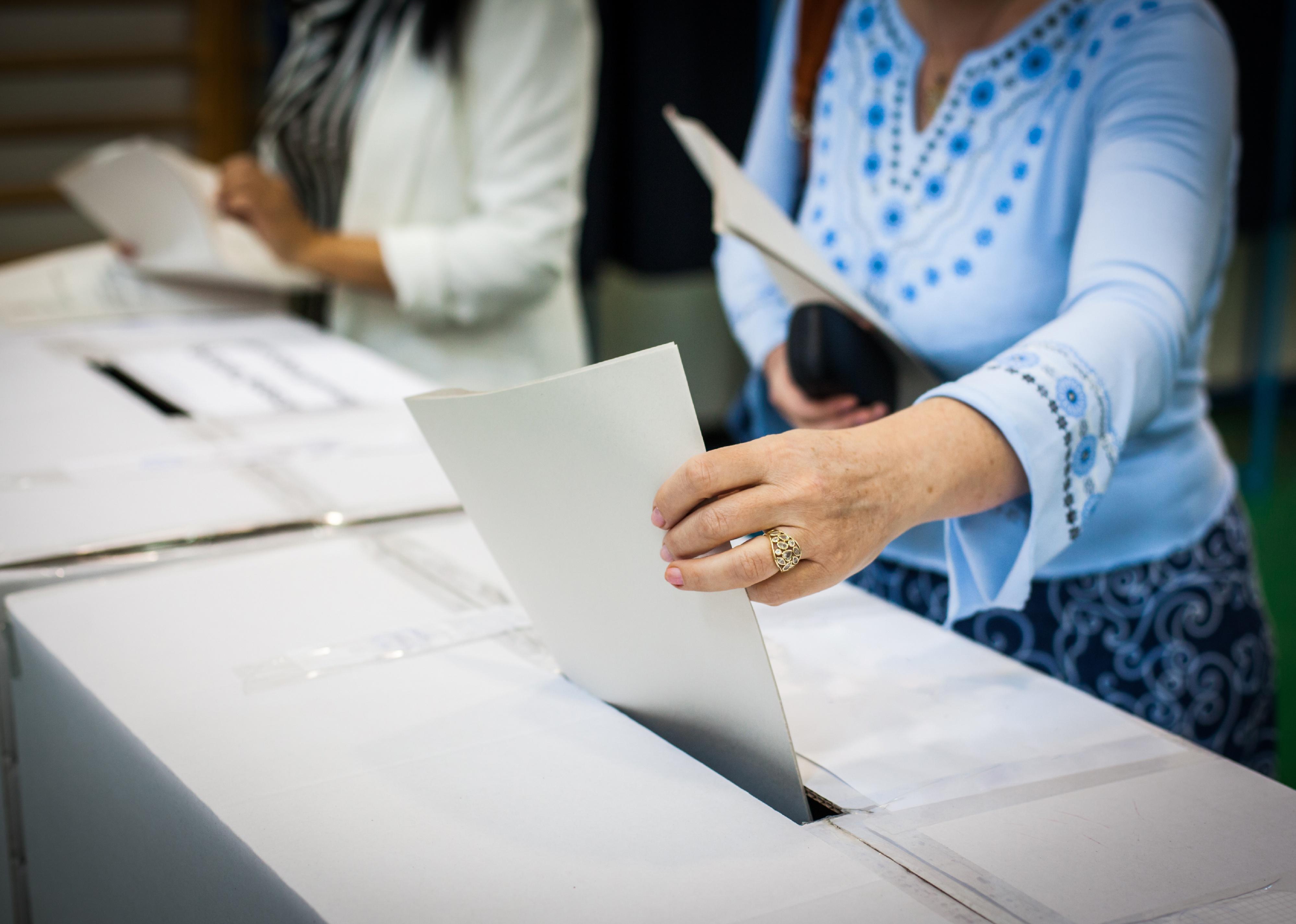 Hand of a person casting a ballot at a polling station during voting