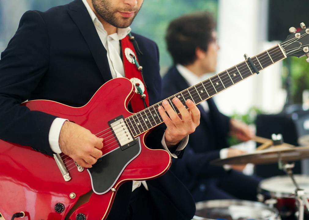Man in black suit plays red guitar standing with a band
