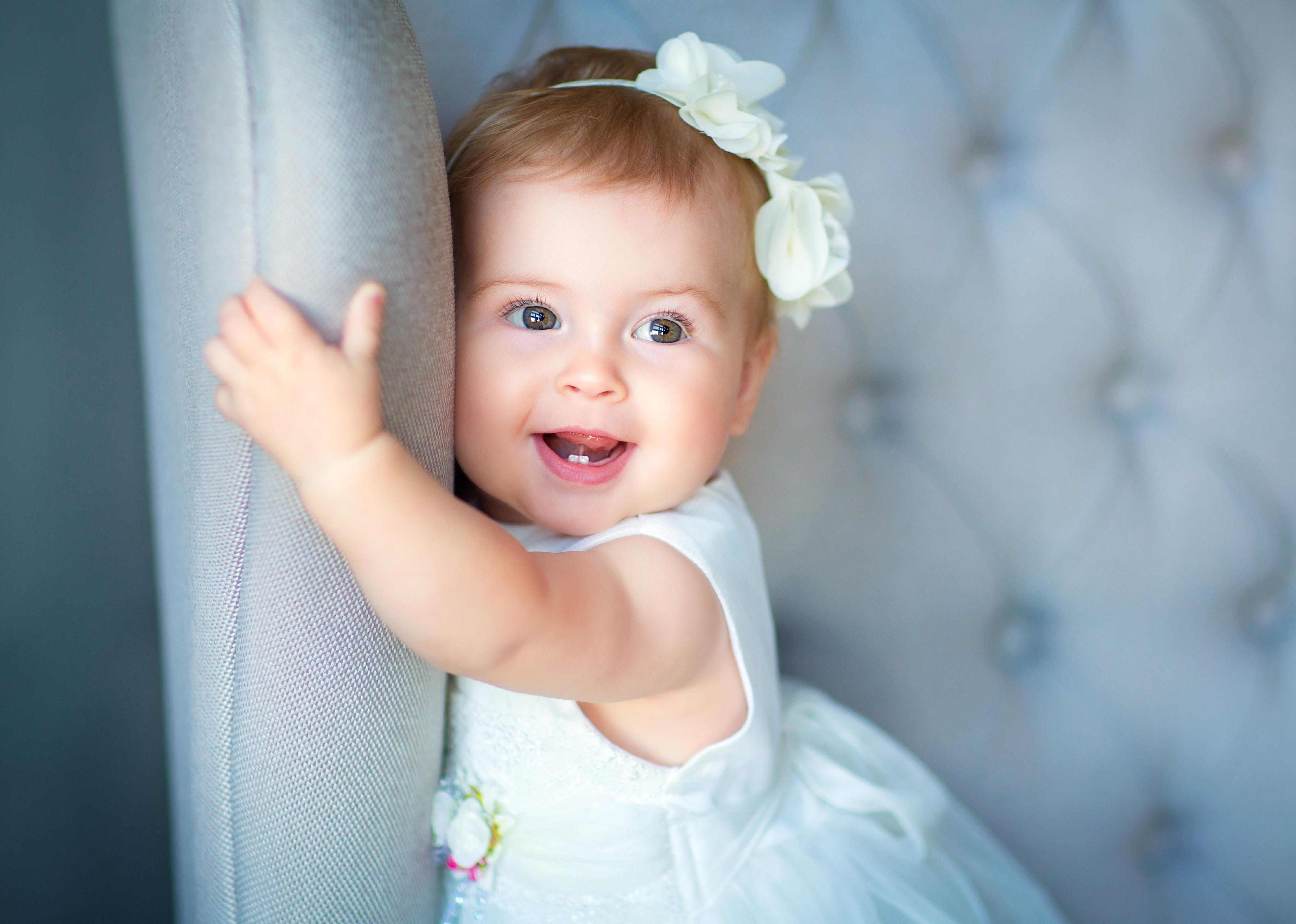 Baby girl wearing white dress and headband.