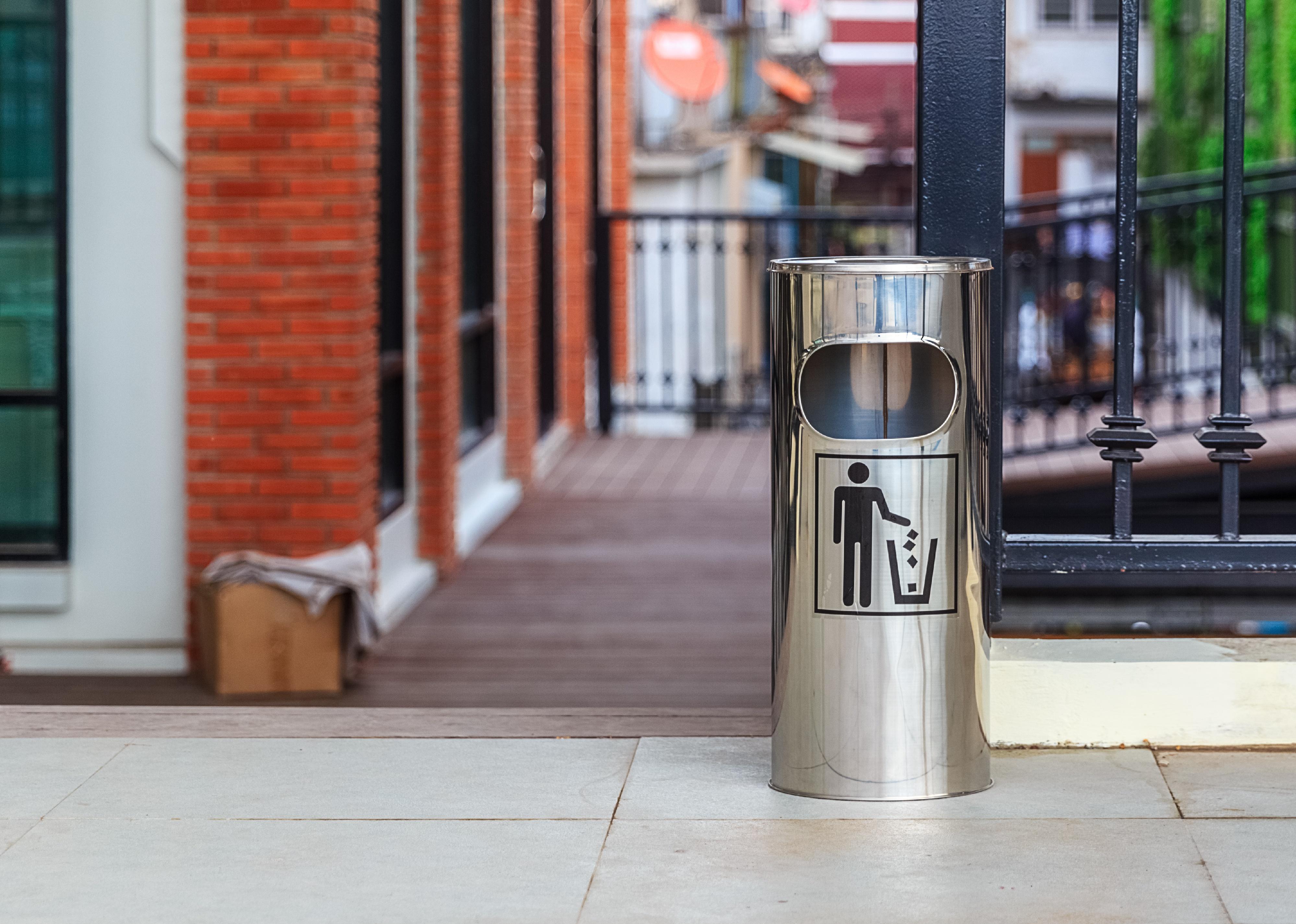 Metal trash can with litter icon in black on a street.