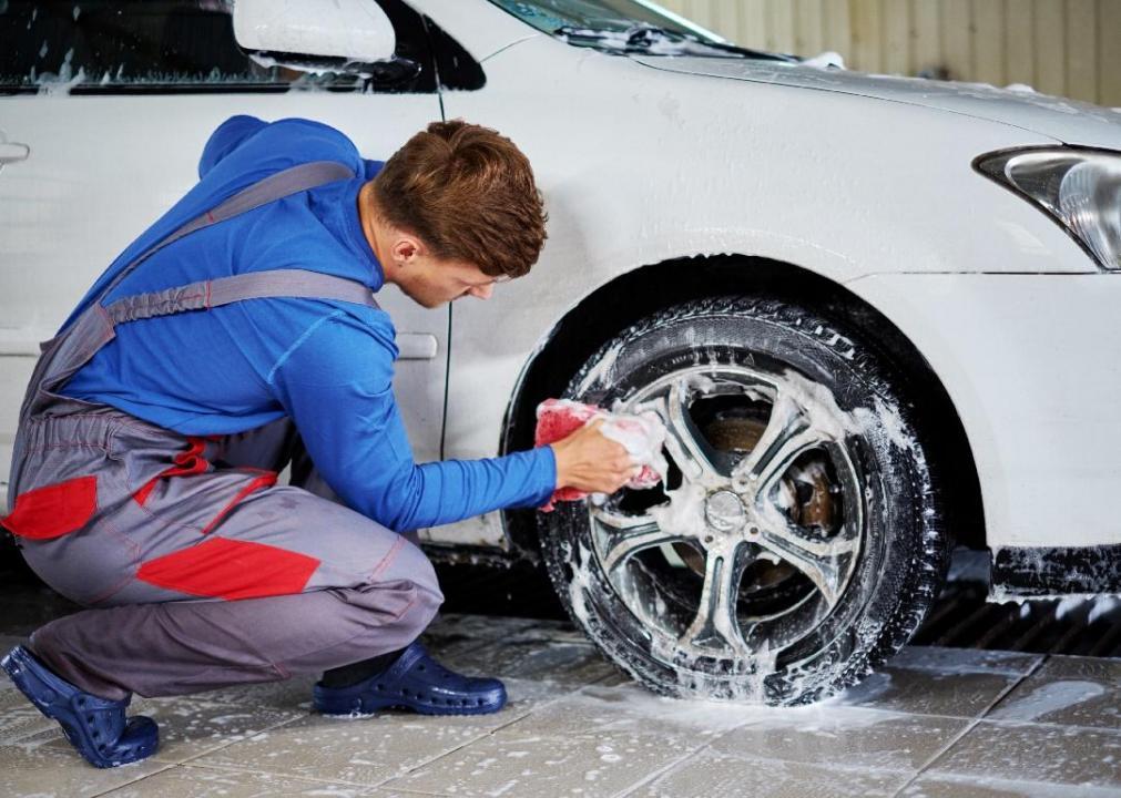 A man washing the tires of a vehicle.