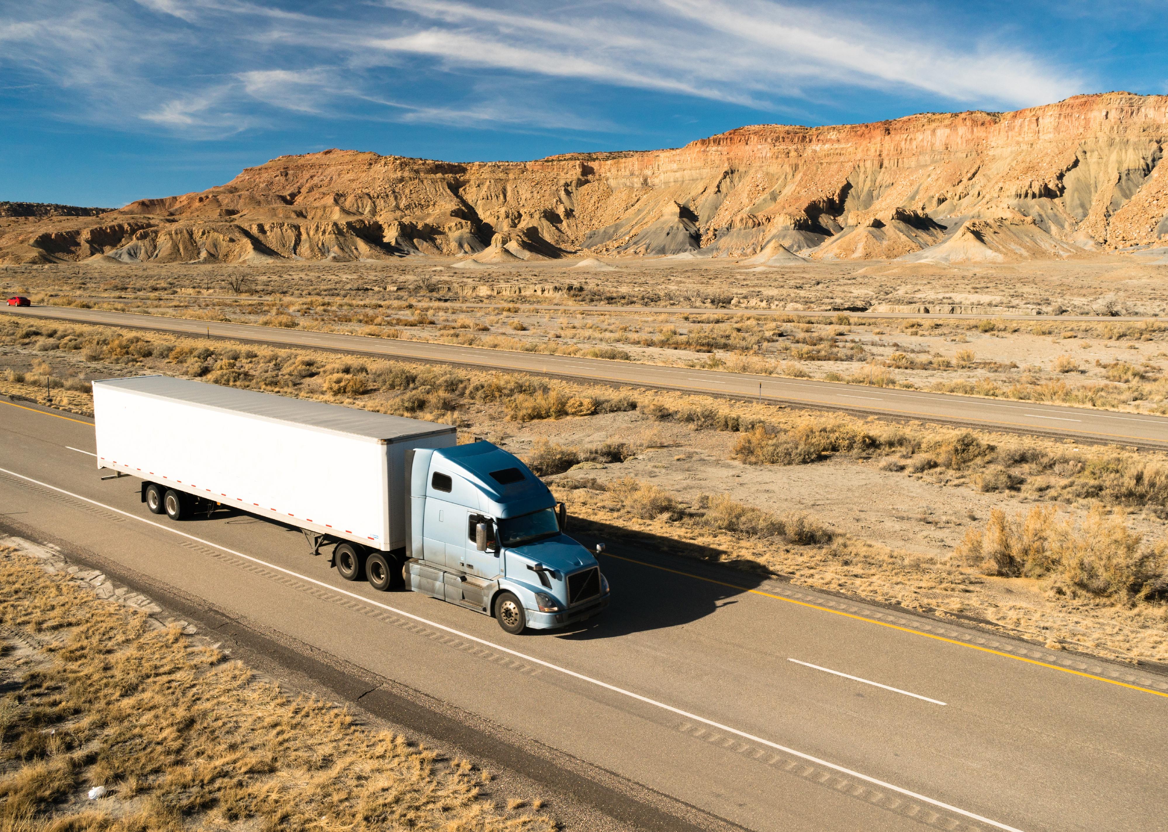 Semitruck on a highway with desert mountains in background.