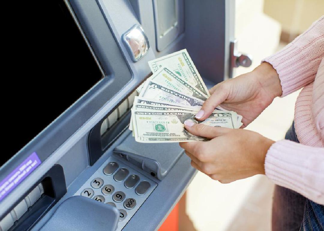 A pair of hands counting money next to an ATM.