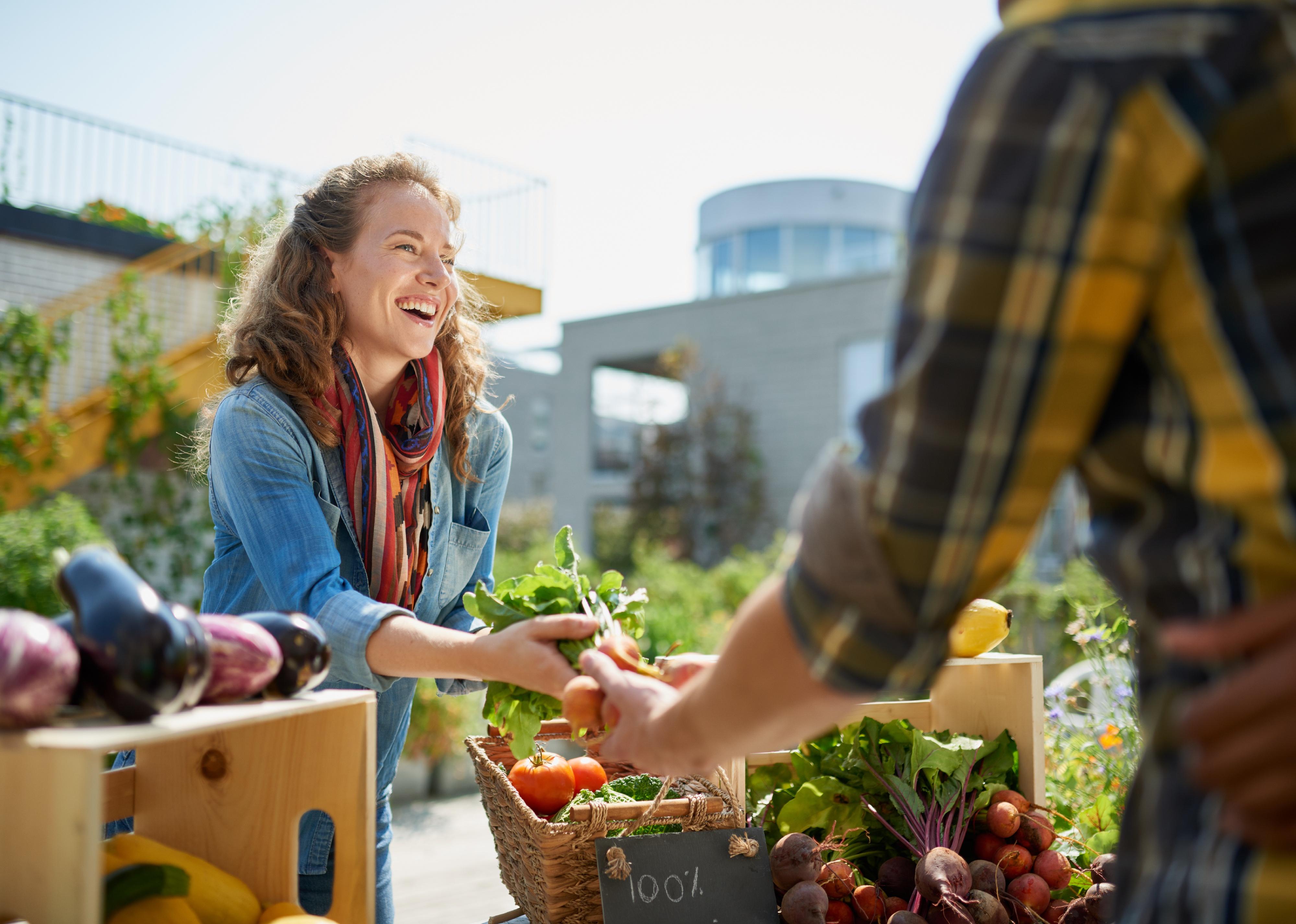 Smiling woman tending a vegetable stall at a farmer