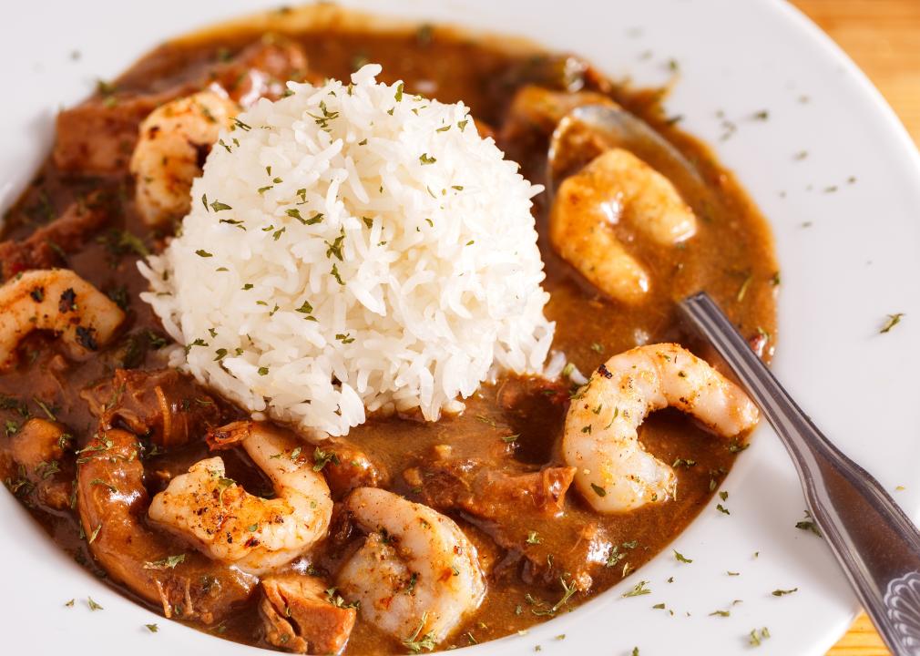 Seafood gumbo with white rice in the middle of the bowl with a spoon.