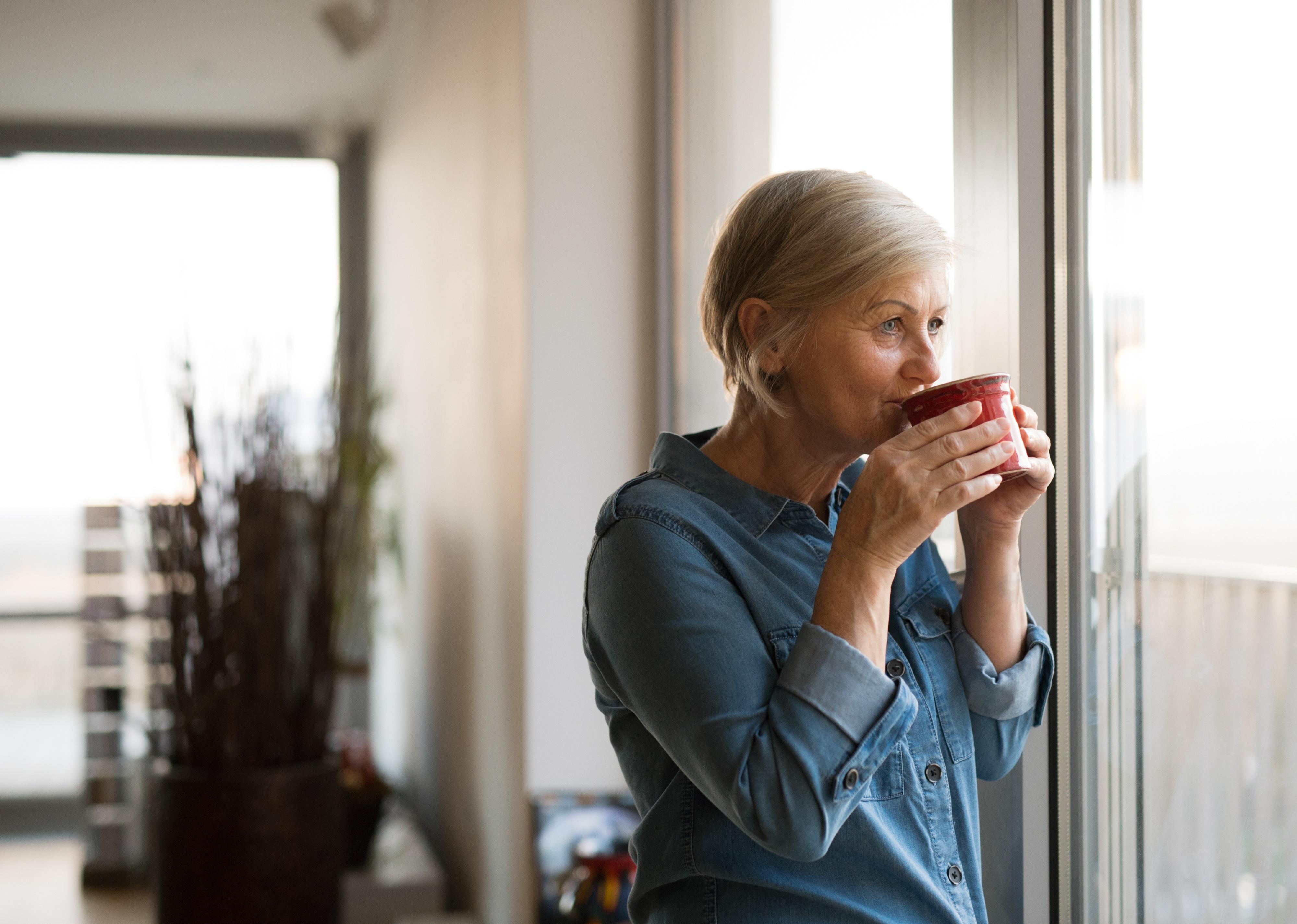 Senior woman at the window holding a cup of coffee.
