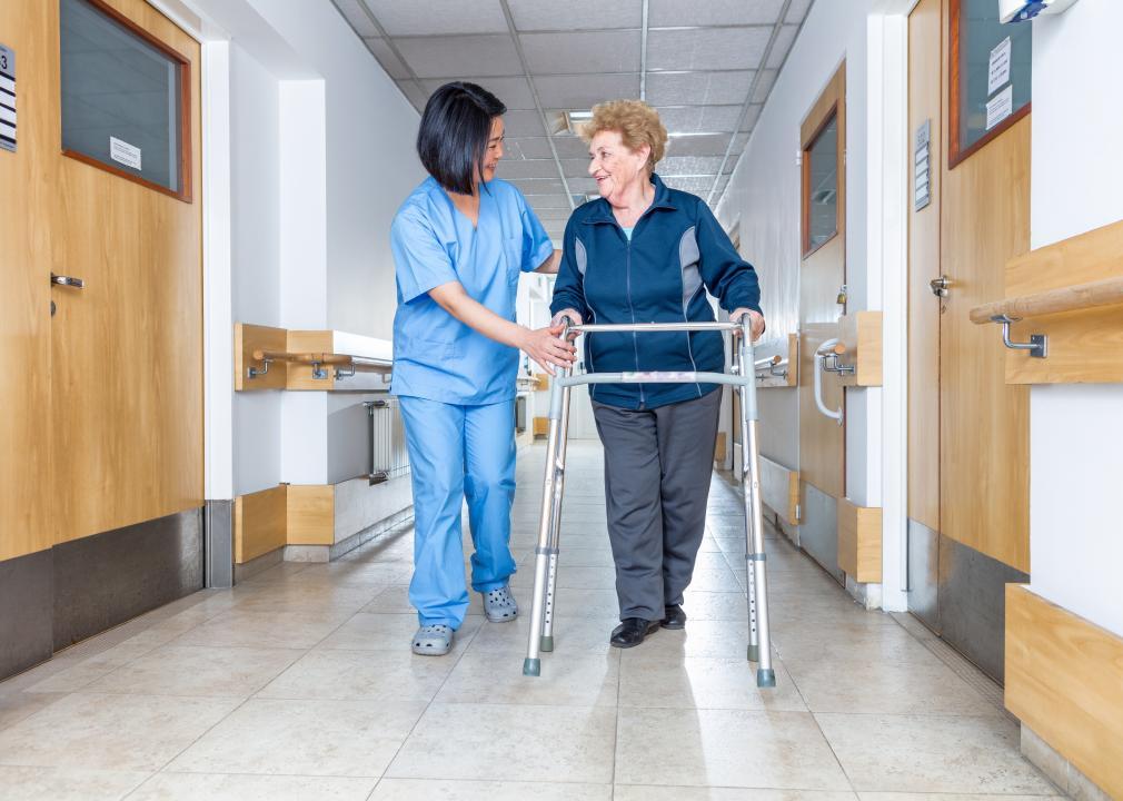 A nursing assistant helps a patient with a walker.