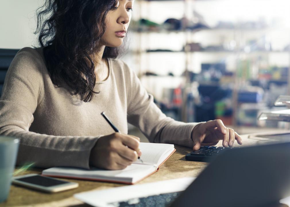 A woman operates a calculator  and enters figures in a log book.