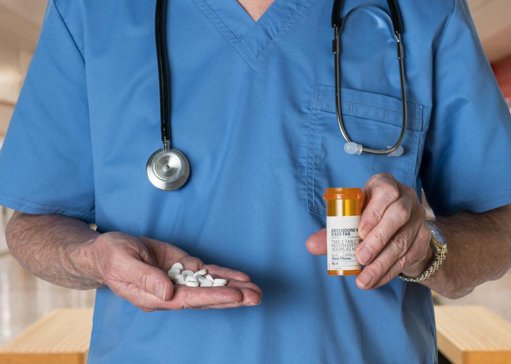 Doctor with stethoscope in scrubs holding bottle and tablets of Oxycodone.