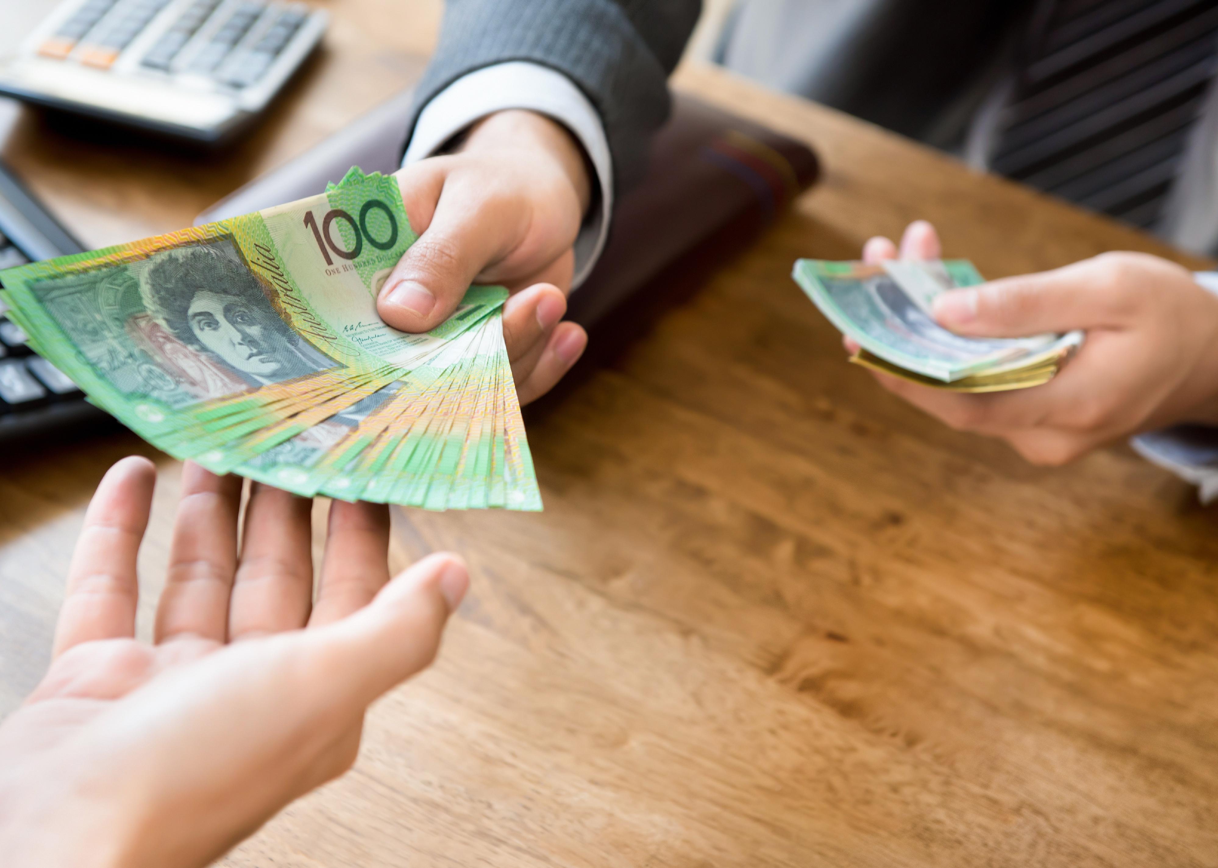 Hands handing over Australian Dollars