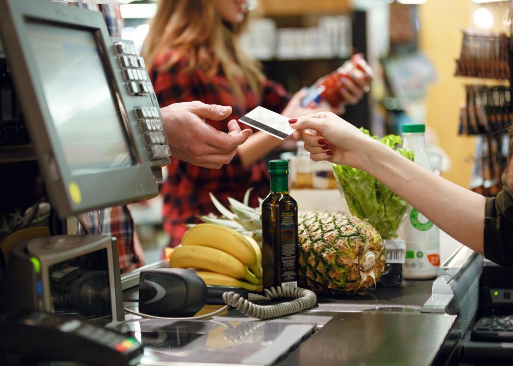 A cashier handing back a credit card to a person in a check out line in a grocery store.