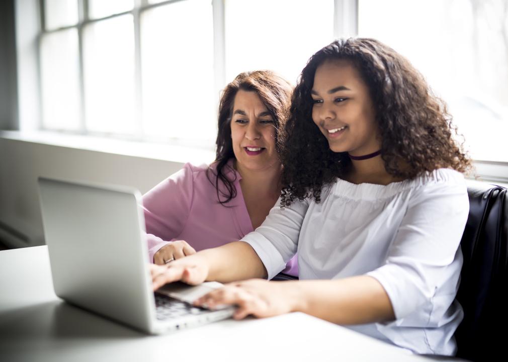 A woman and a teenage girl looking at laptop together.