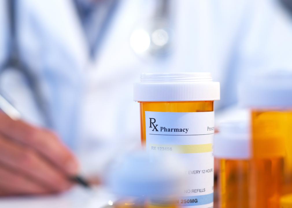 Doctor writing with prescription drug bottle set on the table in front of them.