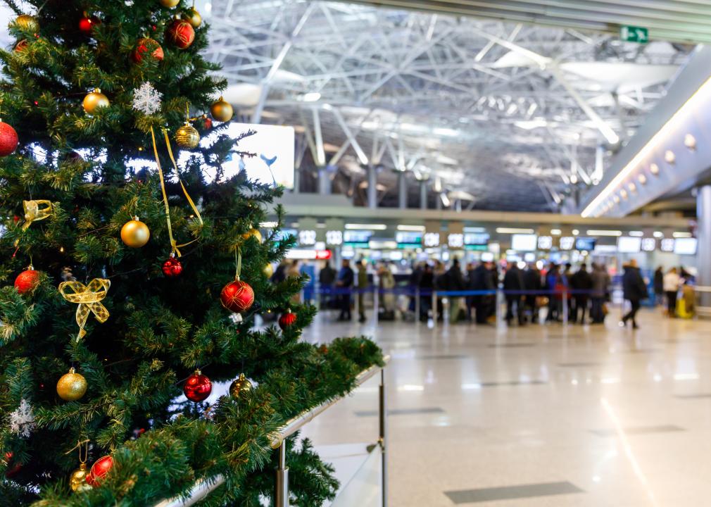 Christmas tree in the airport with people at the check-in counters in the background.