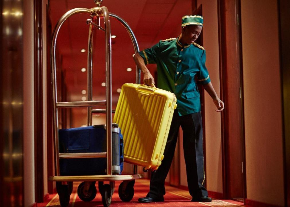 A bellhop takes a suitcase off a cart.