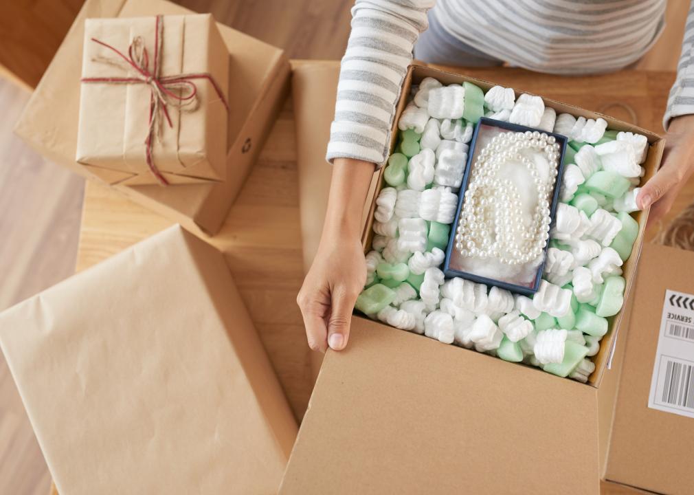 Person opening a shipment of jewelry, with a pearl necklace in a box filled with packing peanuts.