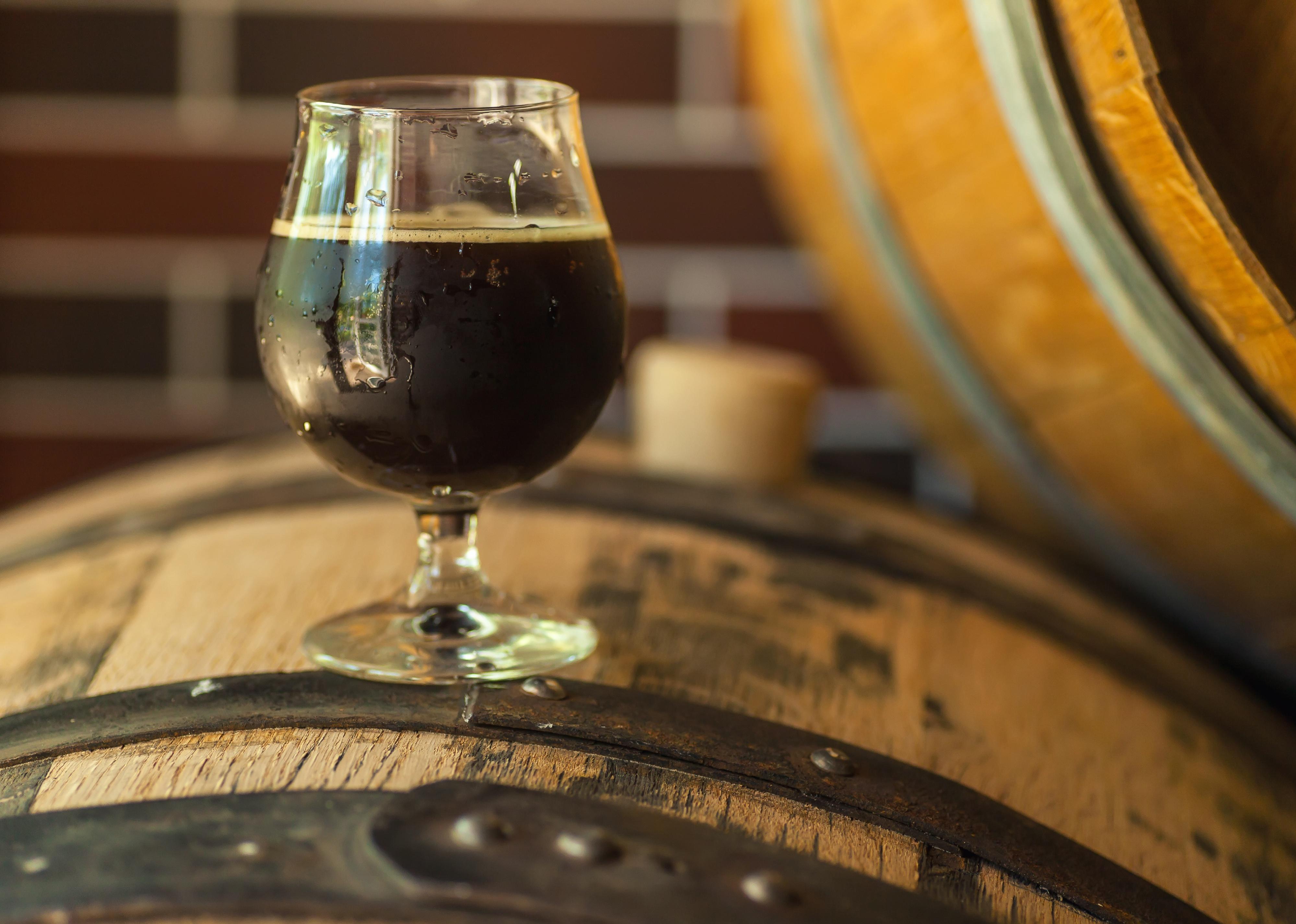 Glass of dark stout beer standing on an oak wood barrel 
