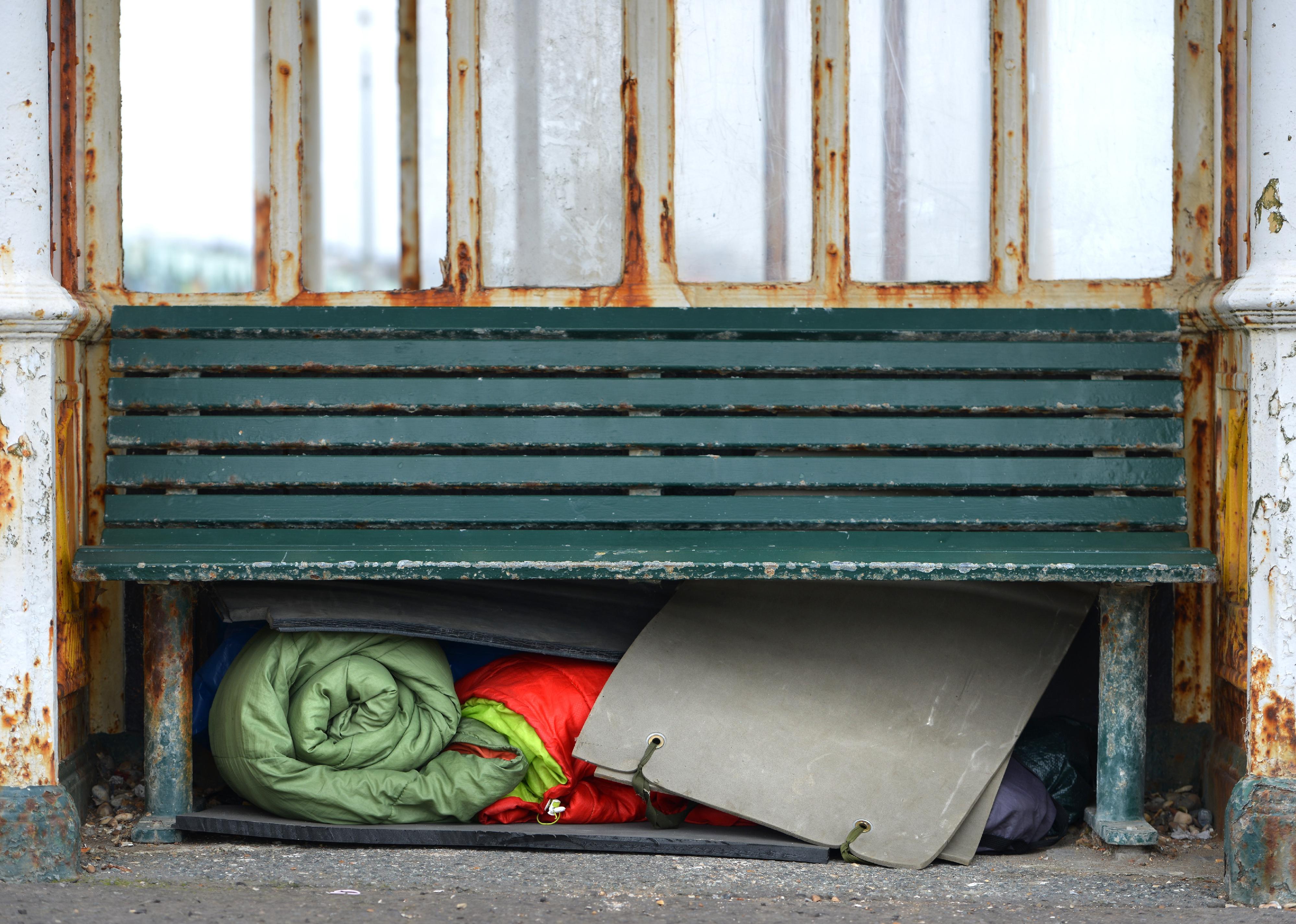 Homeless person's sleeping bags and bedding under a bench.