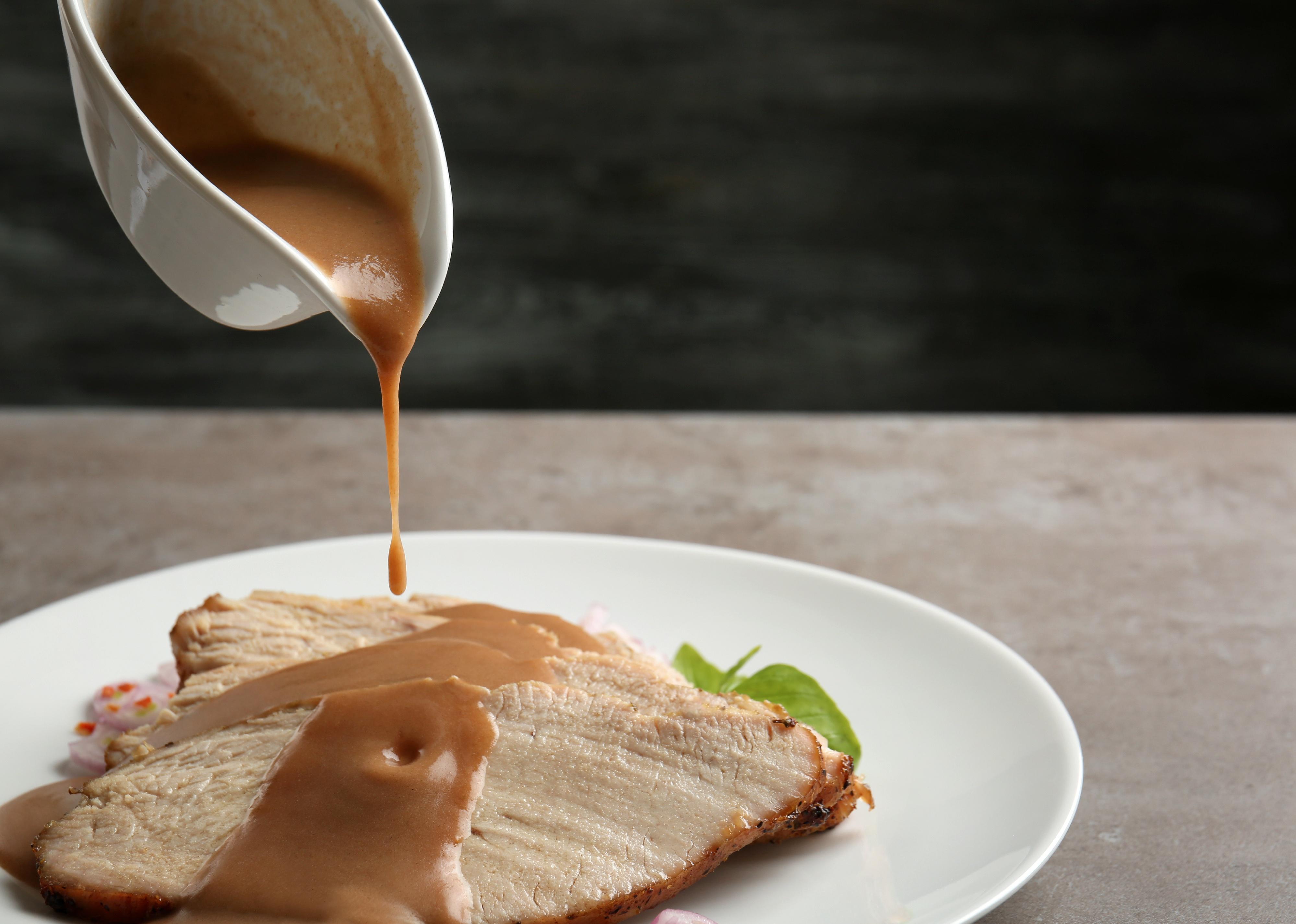 Turkey gravy is poured onto sliced meat on plate against dark background.