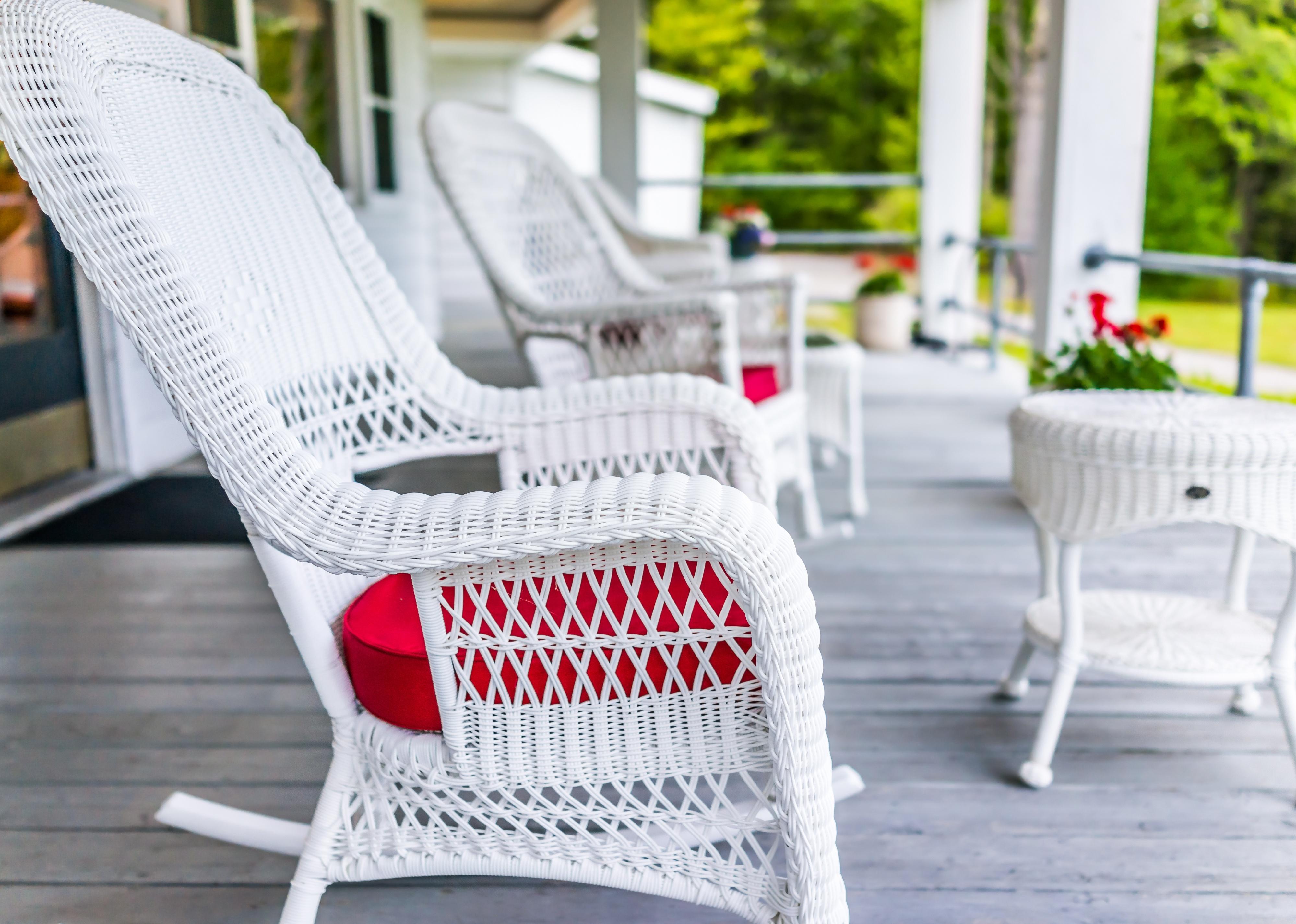 Front porch of house with white rocking chairs on wooden deck.