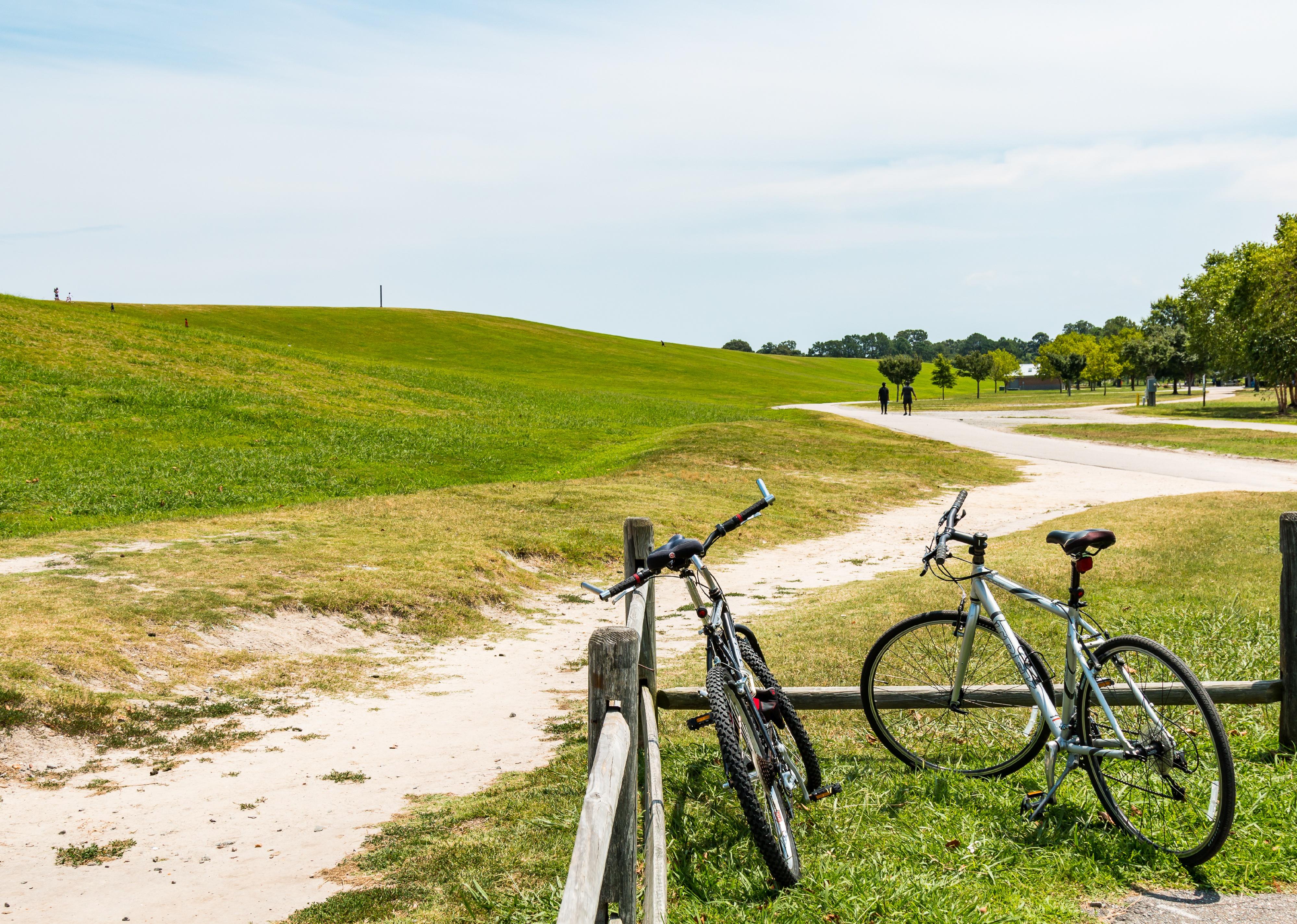 Two bicycles rest on a fence while people trail hike at Mount Trashmore Park.