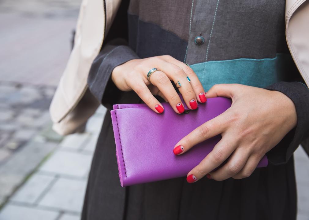 Woman with a bright red manicure and silver rings holds a large purple leather purse