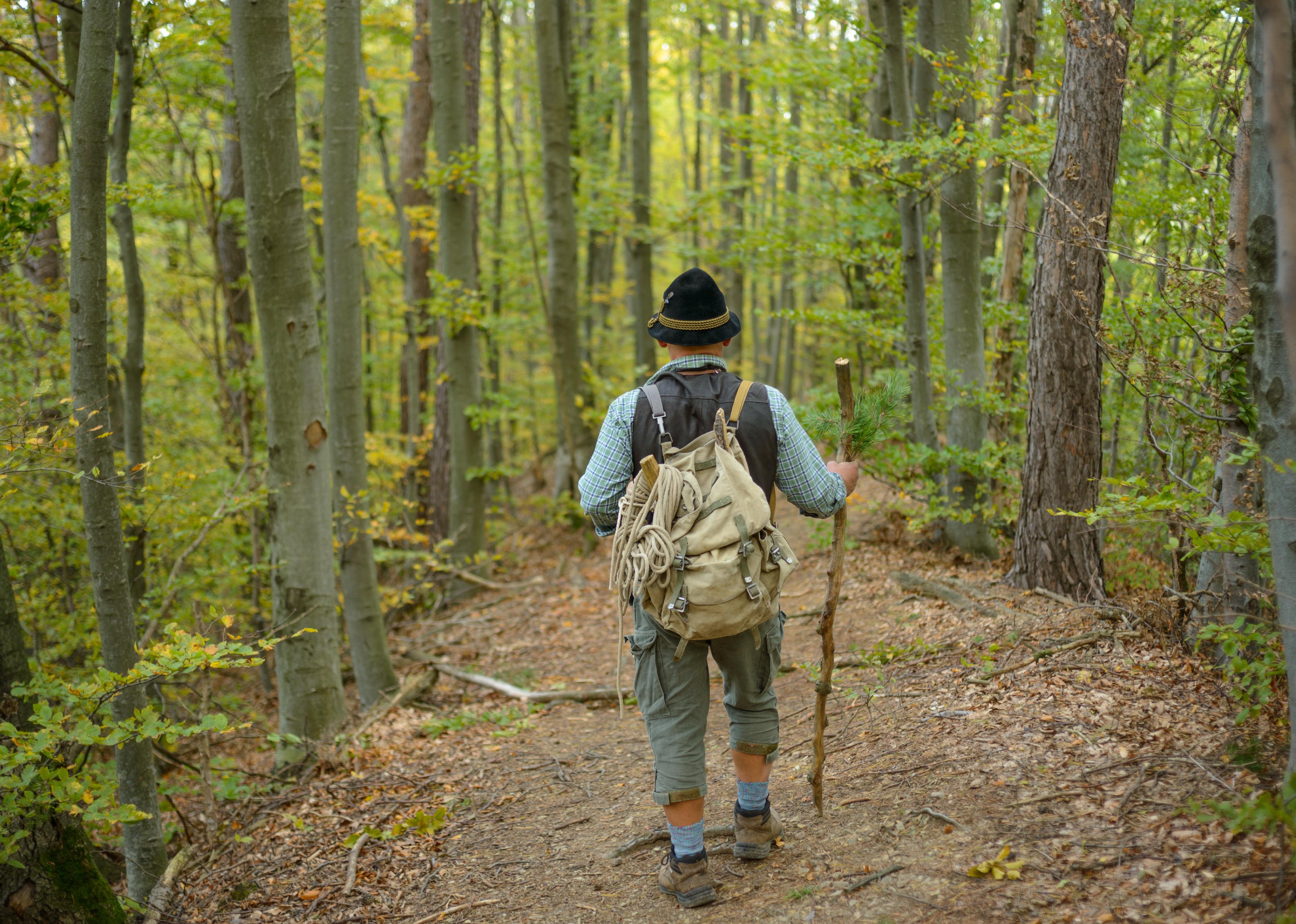 An old man in a hat with a backpack on a trail.