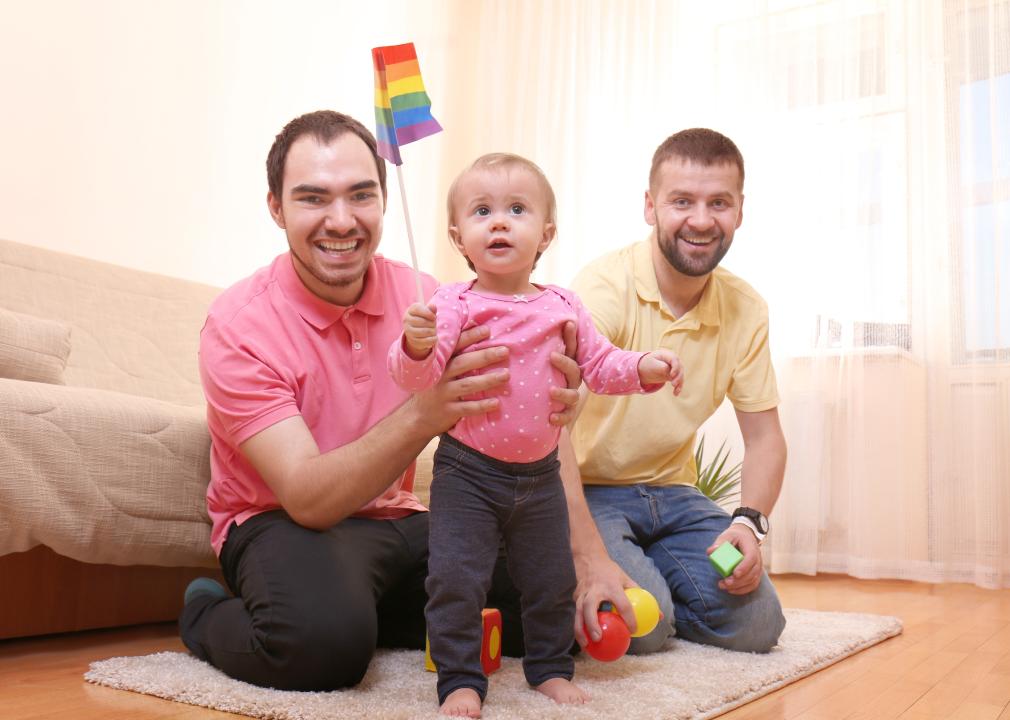 Two men with baby girl holding pride flag 