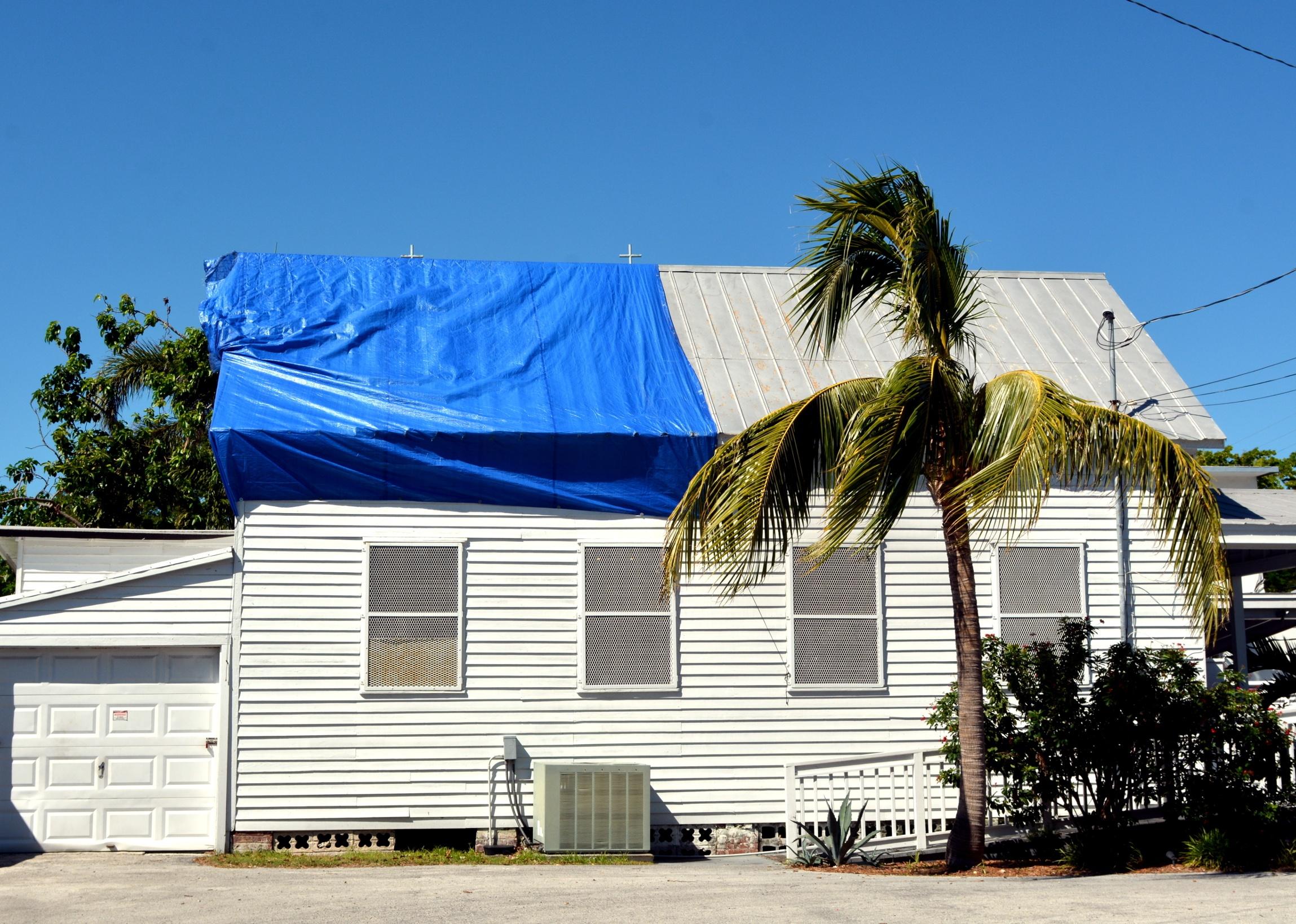 Blue plastic tarpaulin covers roof damage caused by a hurricane.