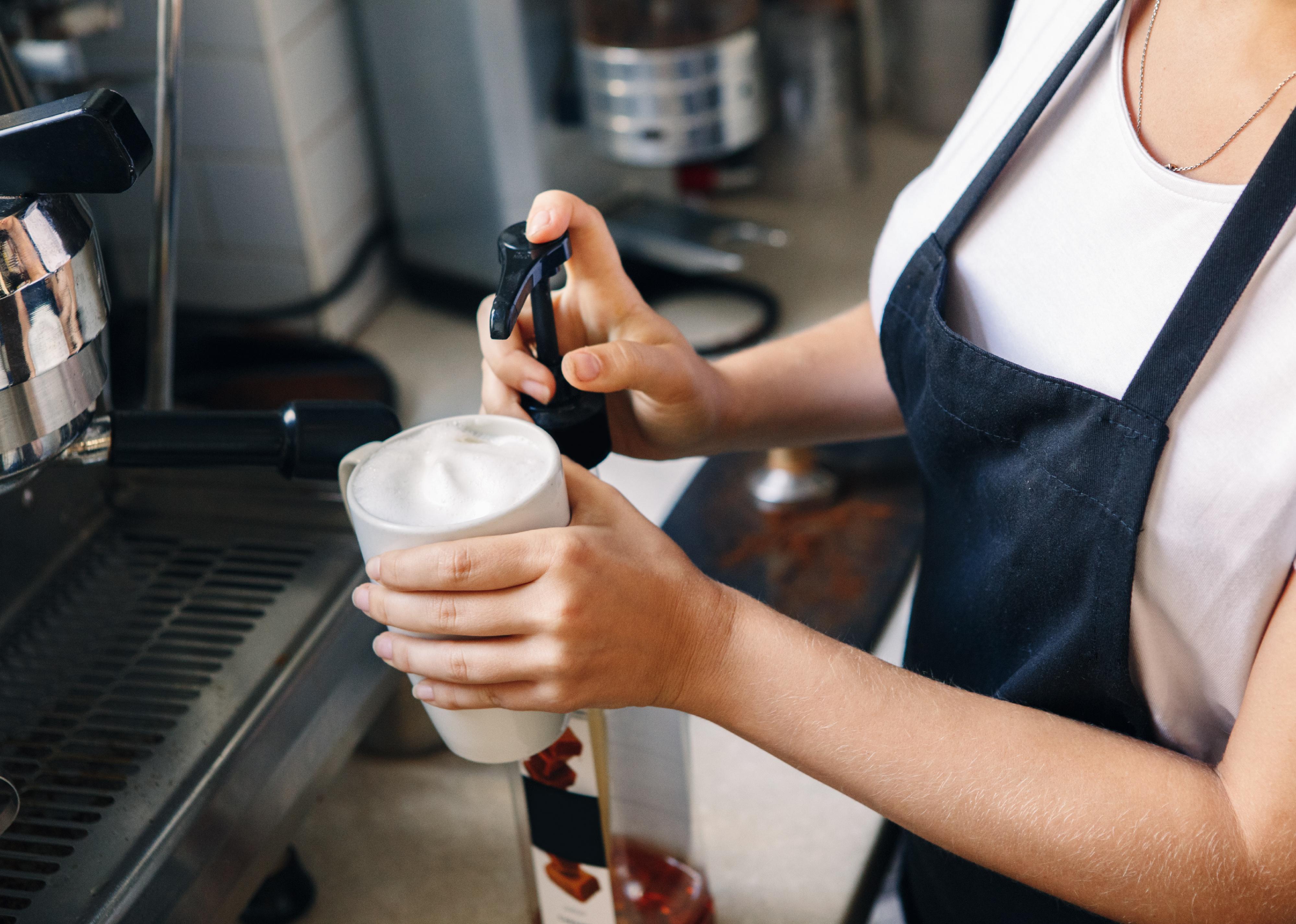 Closeup shot of young barista hands adding flavoured syrup in coffee cup. 