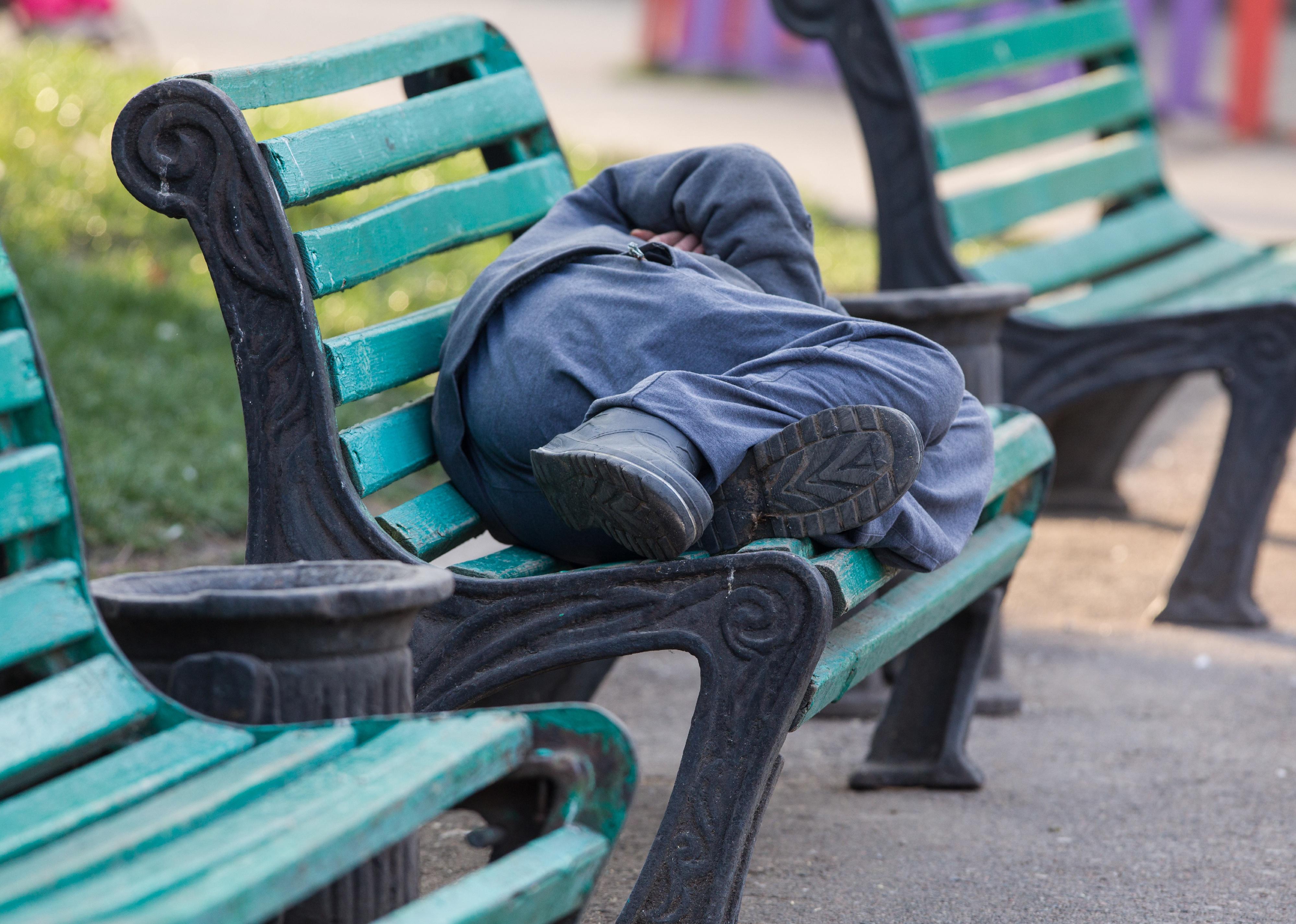 A homeless man sleeping on a bench. 