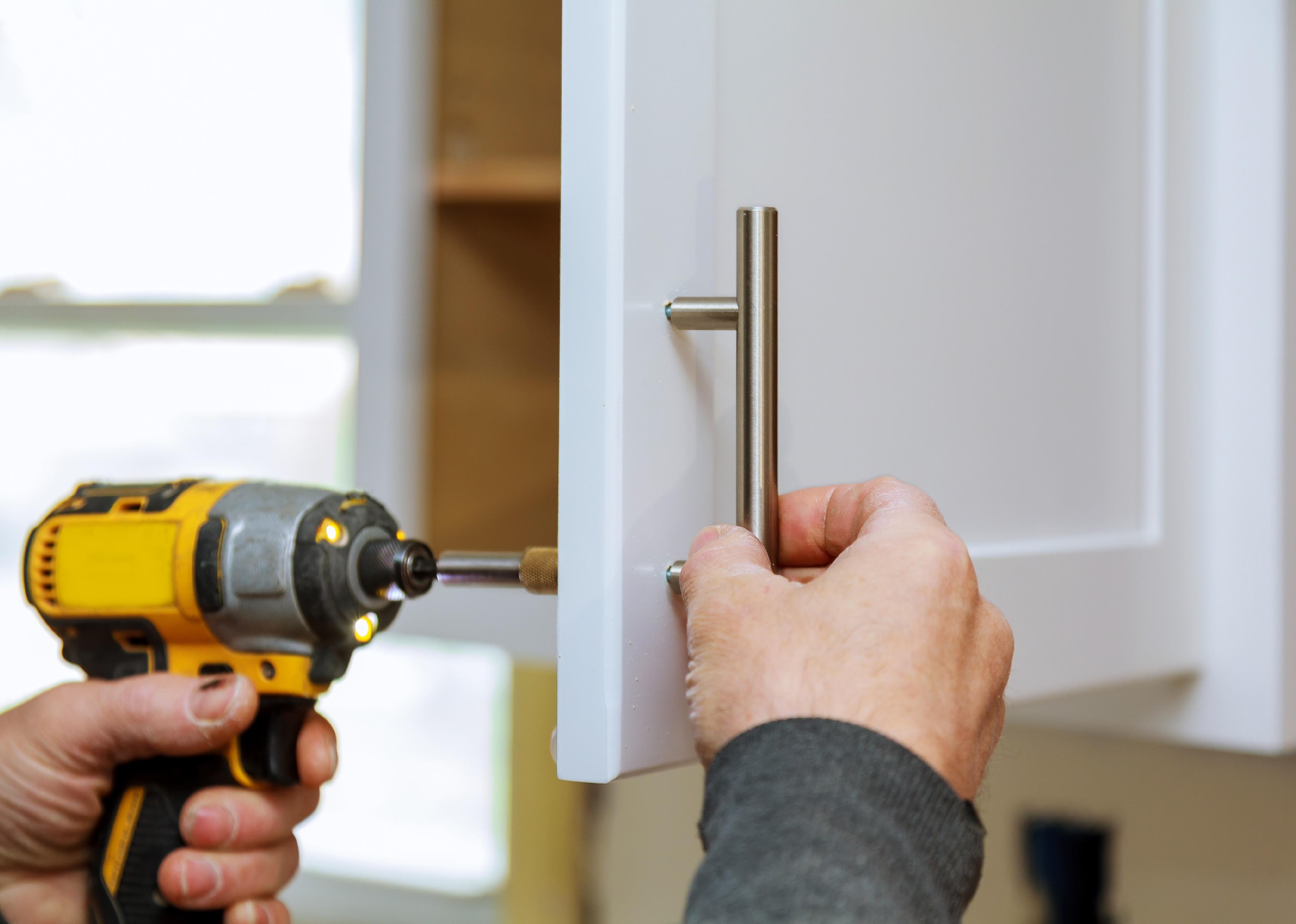 Worker sets a new handle on the white cabinet with a screwdriver