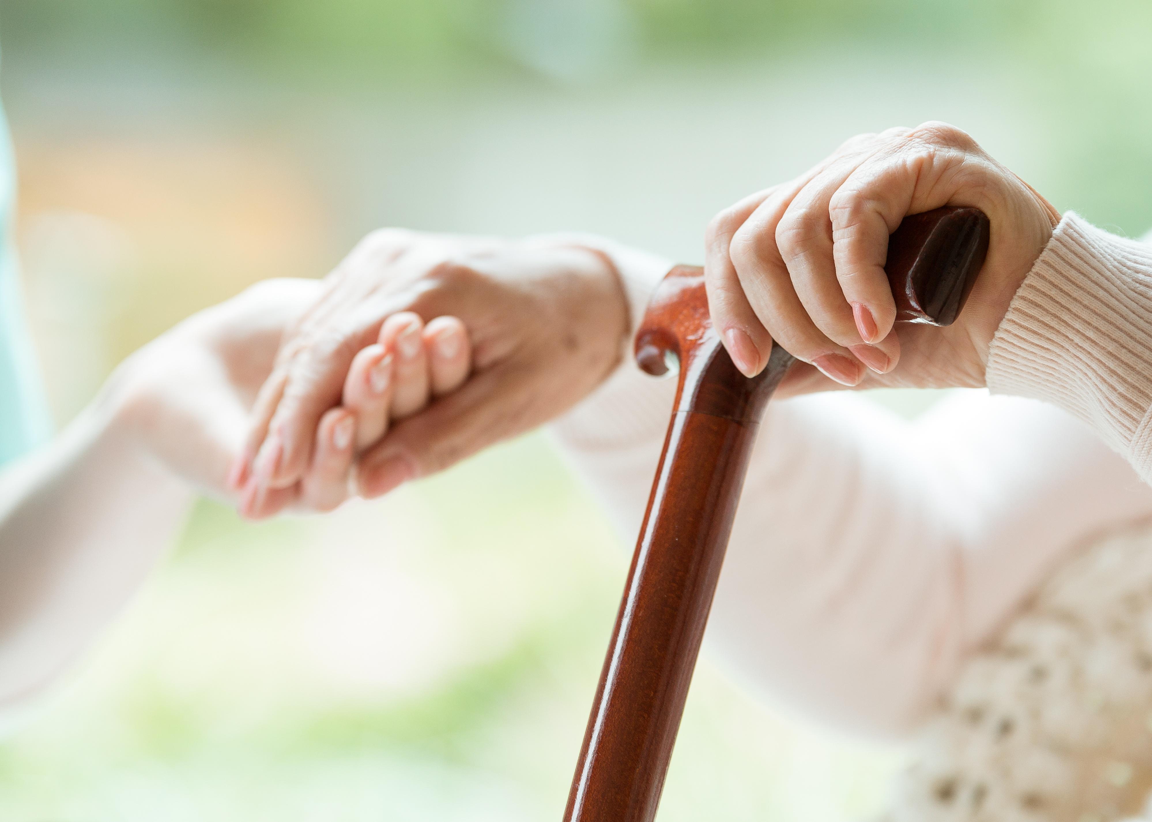 Elderly person using wooden walking cane. 