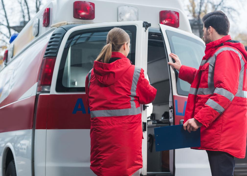 Two professionals wearing neon colored jackets closing the back of an ambulance van.