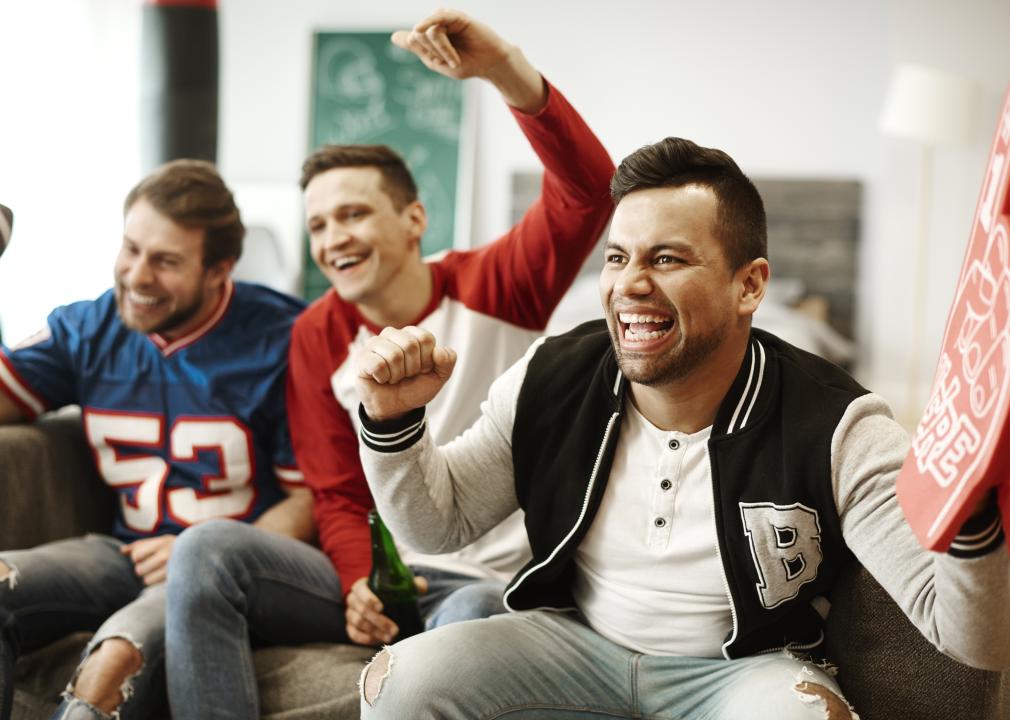 Three men cheering on couch in sports clothing.