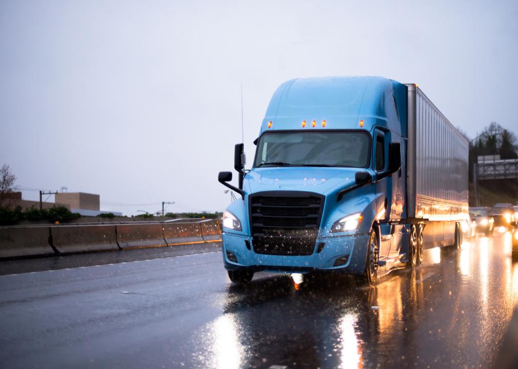 Modern big rig blue semi truck with semi trailer driving on wet highway