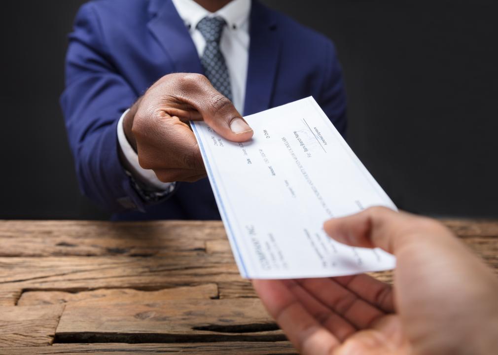 Close-up of a businessperson handing paycheck to colleague over a desk.