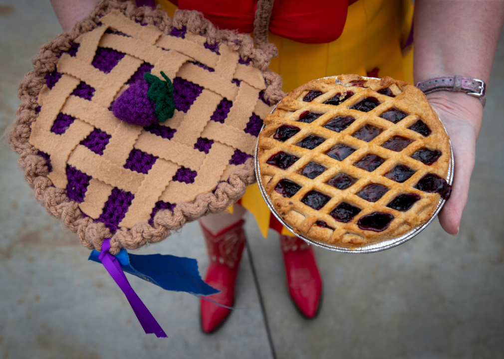 A woman holding a real boysenberry pie next to a knitted pie.