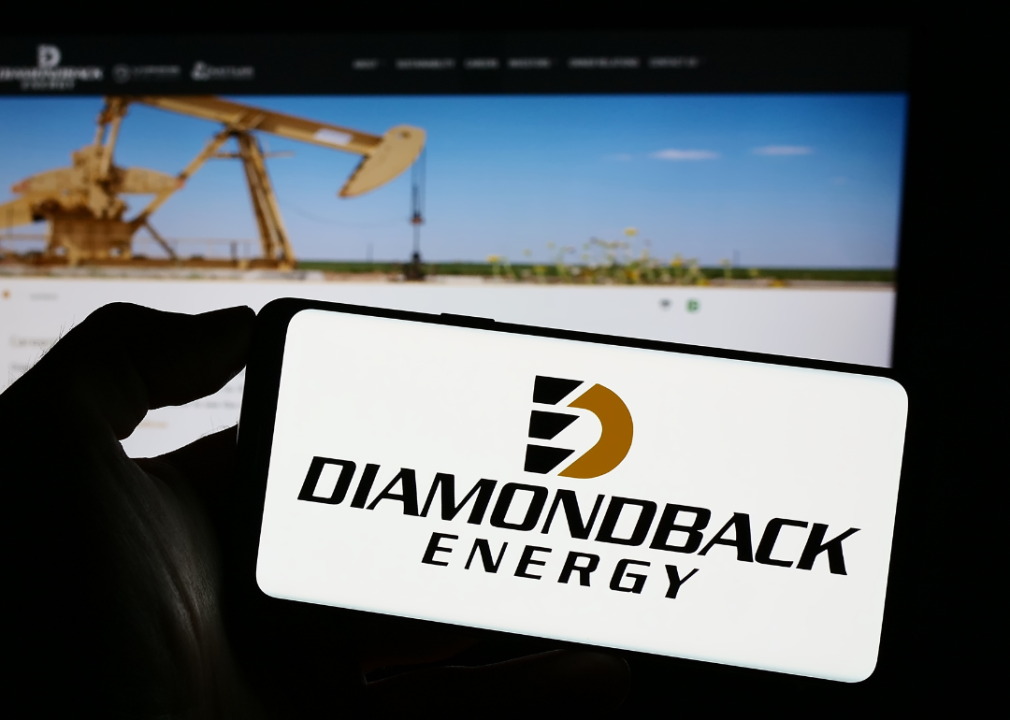 Person holding cellphone with logo of American oil and gas company Diamondback Energy Inc. on screen in front of webpage.