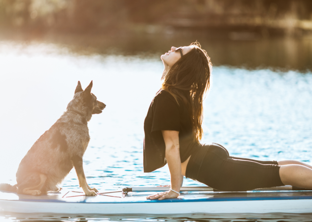 A person doing yoga on a paddleboard with her dog.