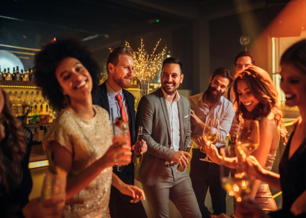 A group of people dressed up in somewhat formal attire having drinks while smiling and chatting..