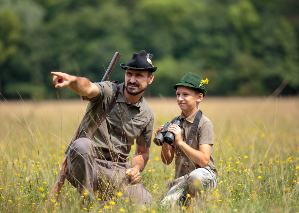 Hunter and young boy with rifles in a field.