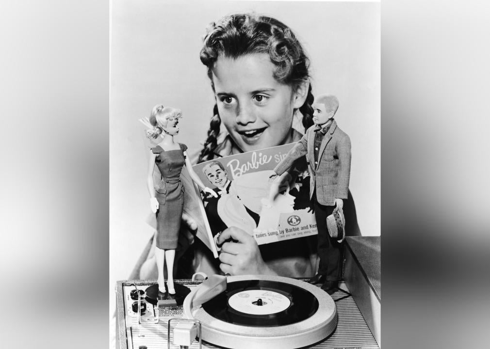 A girl plays with Barbie and Ken dolls and record player.