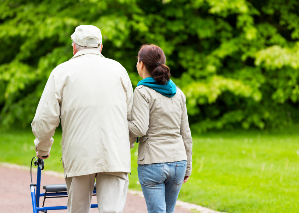 A woman walking with an elderly man using a walker.