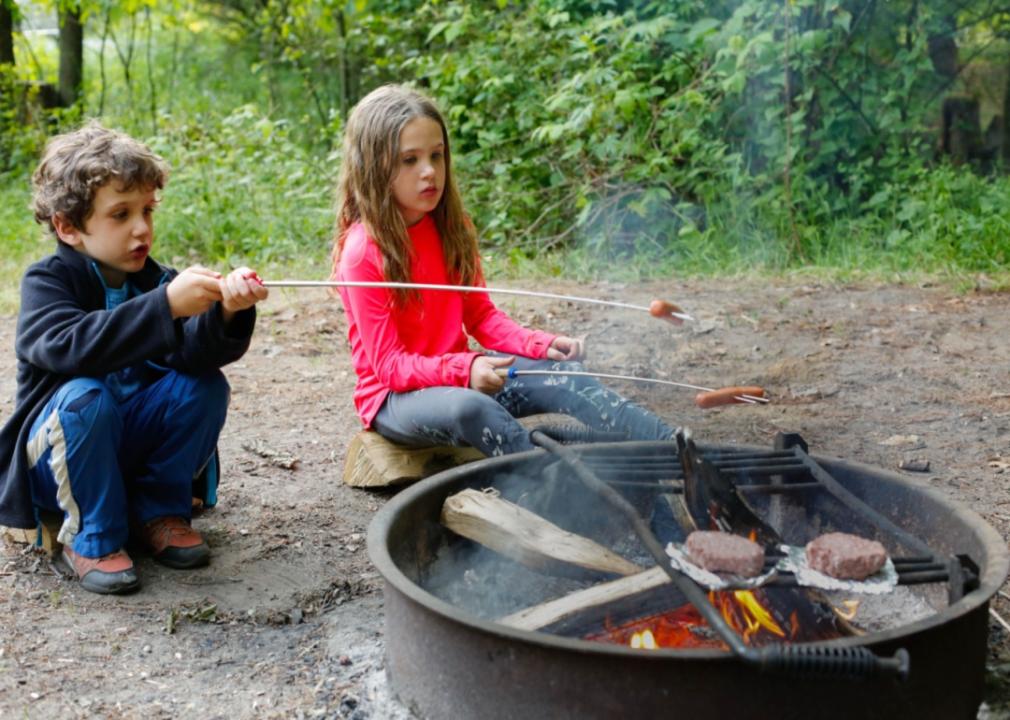 Kids roasting hotdogs on a fire.