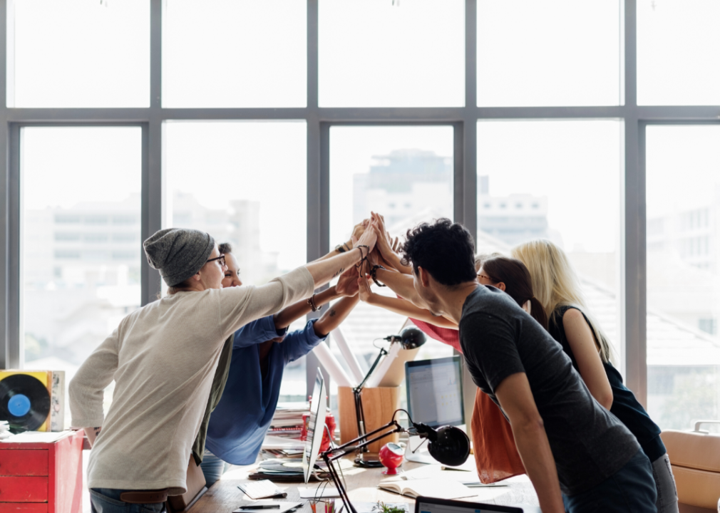 Employees giving a group high five in a brightly lit office.