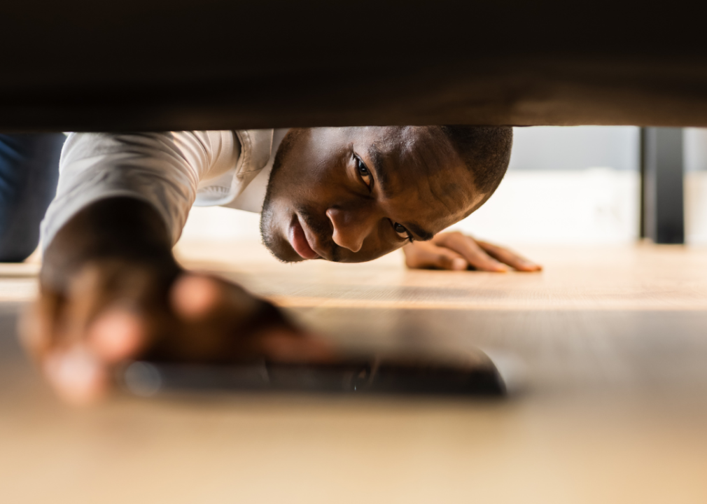 A man pulling a phone out from under a couch.