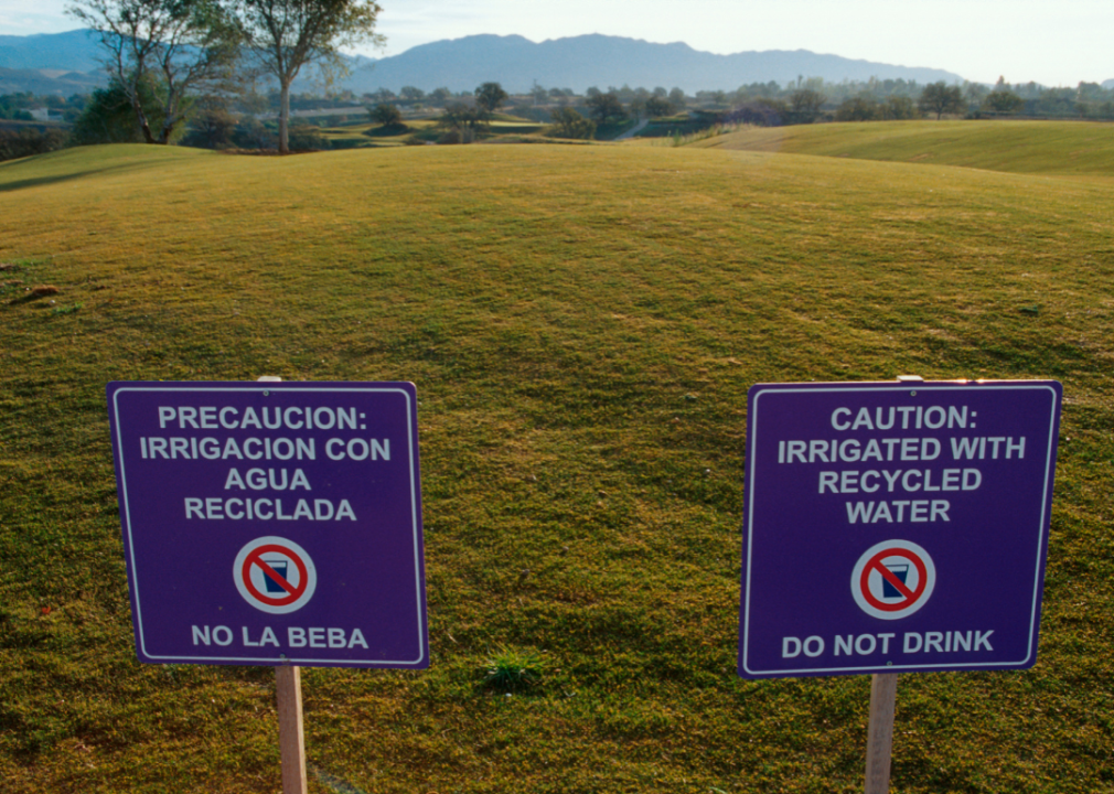 Two signs, one in English and one in Spanish, that say, caution: irrigated with reccyled water, do not drink.